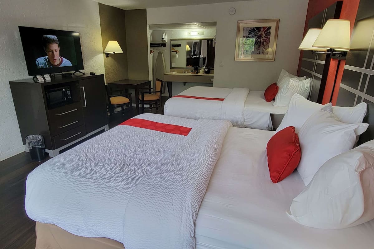 A hotel room with two beds, a TV, a desk, and a mirror.