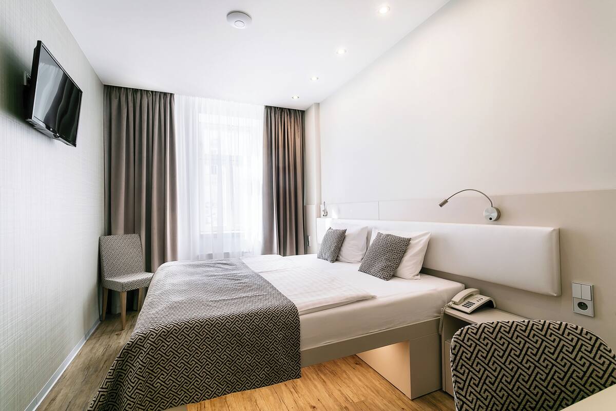 A modern hotel room with a large bed, a TV mounted on the wall, a bedside telephone, and a chair.