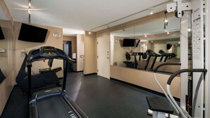 Uma academia com esteira, equipamentos de ginástica e espelhos.