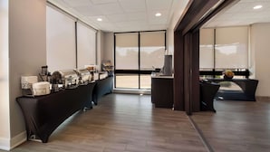 Um saguão de hotel moderno com um balcão de recepção extenso, uma estação de café e uma área de estar com vista para o exterior.