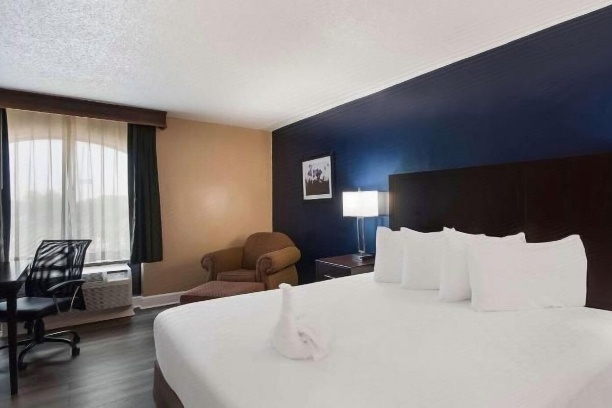 Habitación de hotel con una cama grande, un escritorio, una silla y una ventana con cortinas.