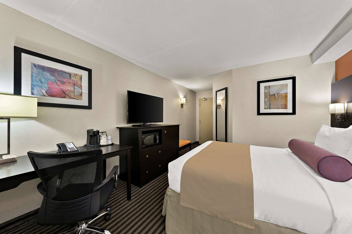 Een hotelkamer met een bed, een bureau met telefoon, een televisie, een dressoir en twee ingelijste kunstwerken aan de muur.