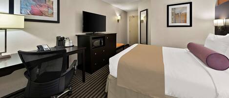 A hotel room with a bed, a desk with a telephone, a television, a dresser, and two framed artworks on the walls.