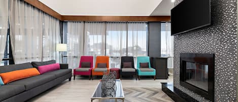 A modern living room with a sofa, colorful chairs, a coffee table, and a large TV on the wall.