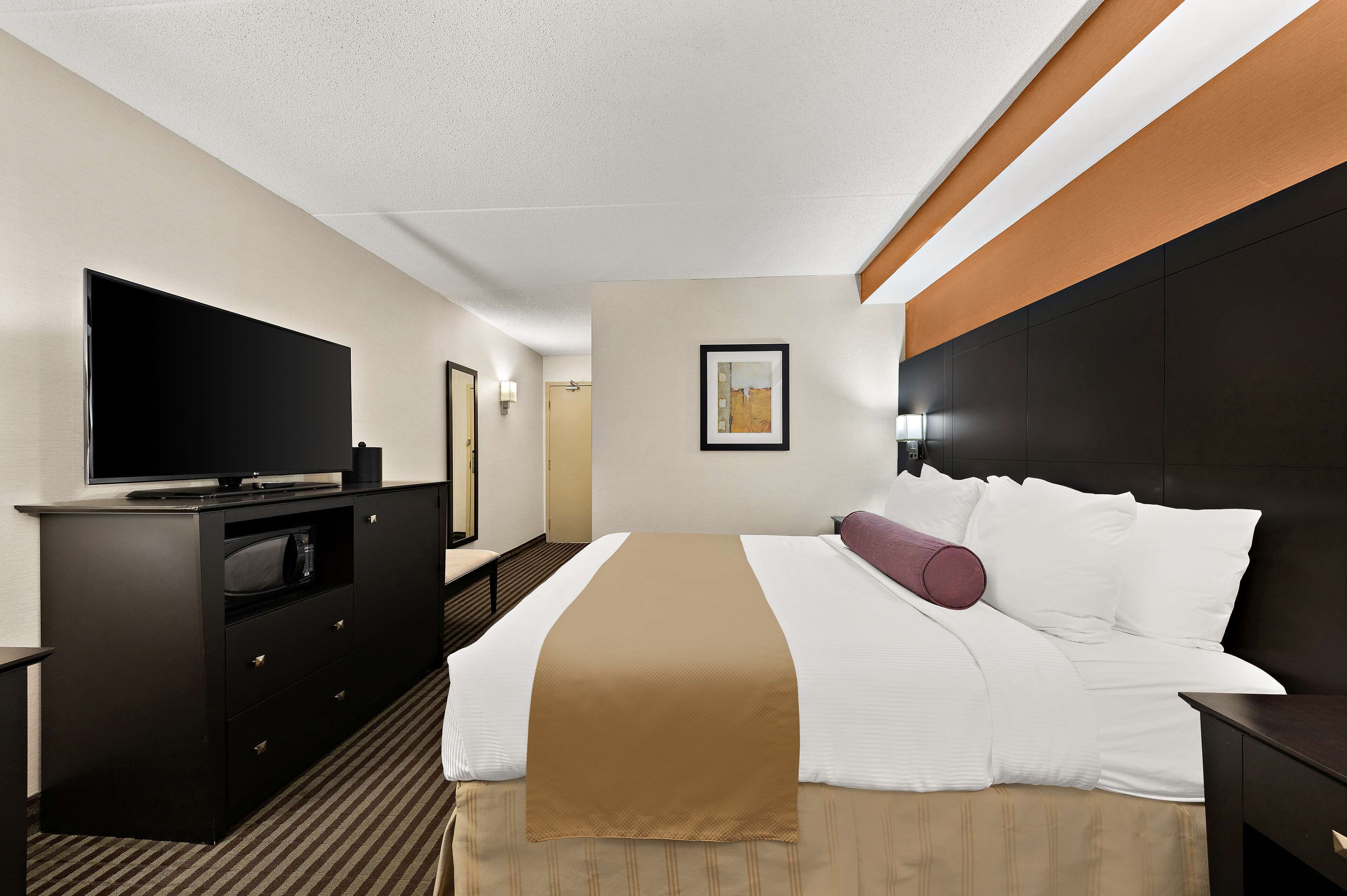 A hotel room with a bed, a flat-screen TV, a dresser, and a framed picture on the wall.