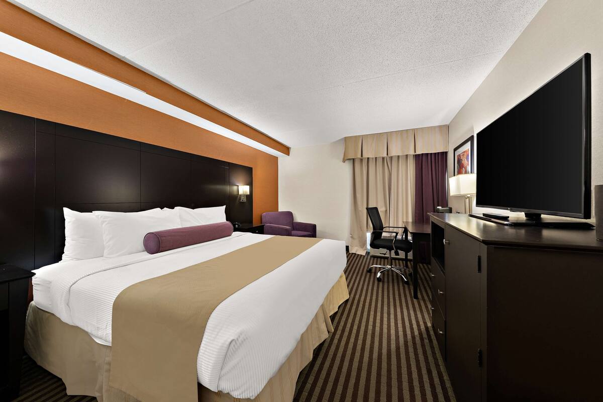 Una habitación de hotel con una cama grande, un escritorio, una silla, un televisor y un armario.