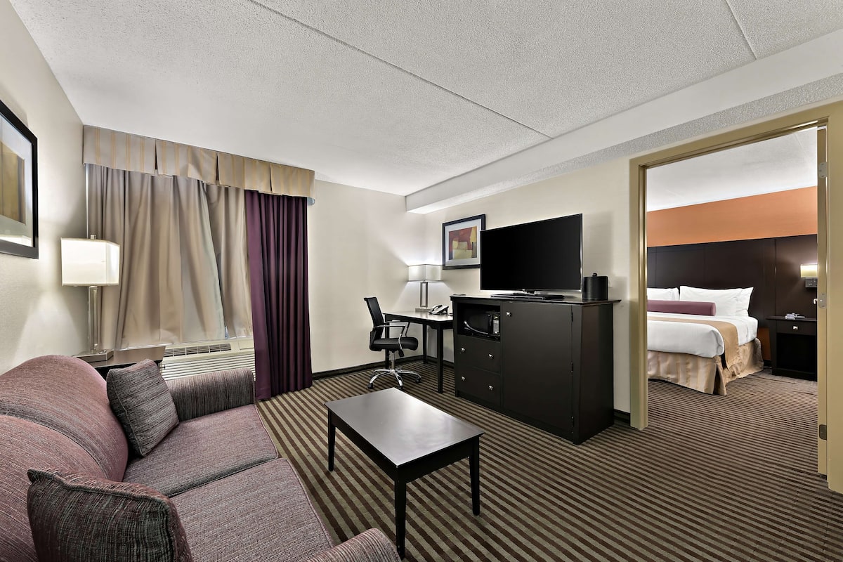 Habitación de hotel con sofá, escritorio, televisor, cama y puerta que da a otra habitación.