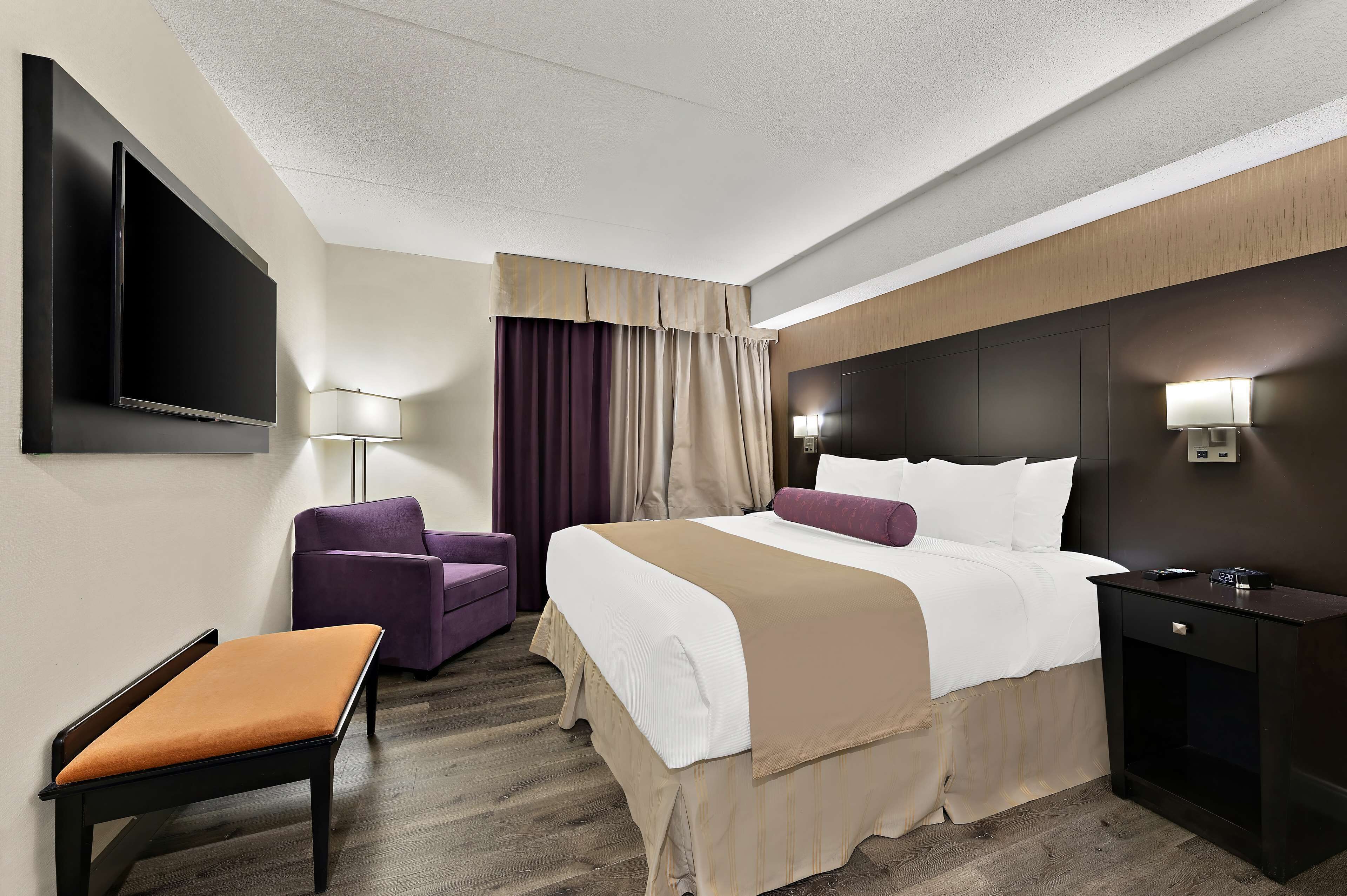 A hotel room with a bed, a chair, a desk, a TV, and a lamp.