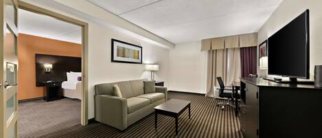 A hotel room with a bed, a sofa, a desk, a television, and a lamp.