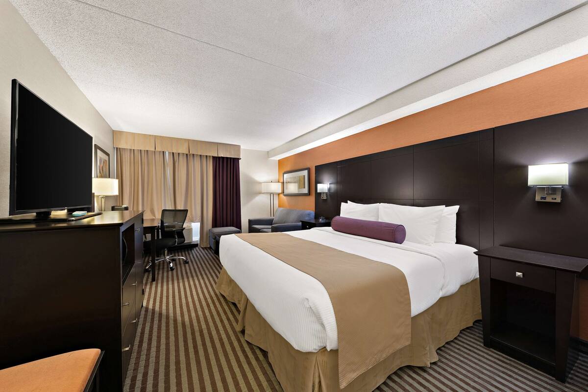 Habitación de hotel con una cama grande, un escritorio con computadora, televisor y una zona de estar con una silla y un sofá.