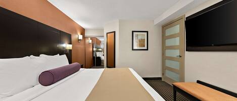 Ein Hotelzimmer mit einem großen Bett, einer Sitzbank, einem Fernseher und einer Tür zu einem Badezimmer.