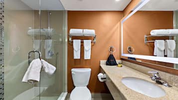 A modern bathroom with a glass-enclosed shower, a white toilet, a sink with a mirror, and towels on a rack.