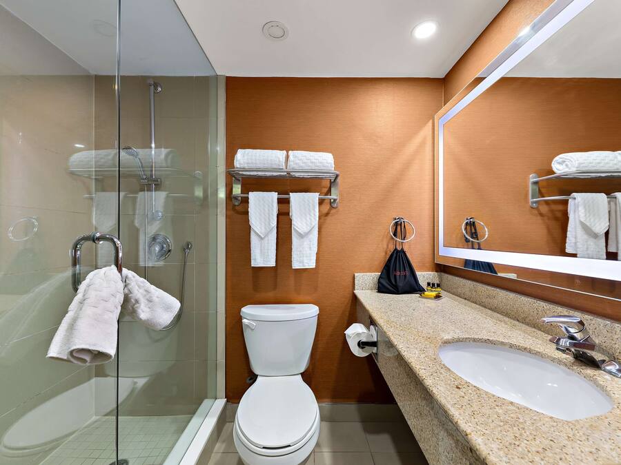 A modern bathroom with a glass-enclosed shower, a white toilet, a sink with a mirror, and towels on a rack.