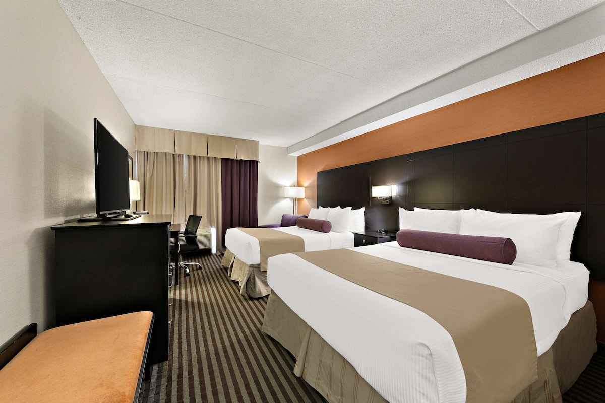 Een hotelkamer met twee bedden, een bureau met een televisie, een lamp en een stoel.