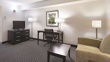 A hotel room with a TV, a desk, a chair, a sofa, and two lamps.