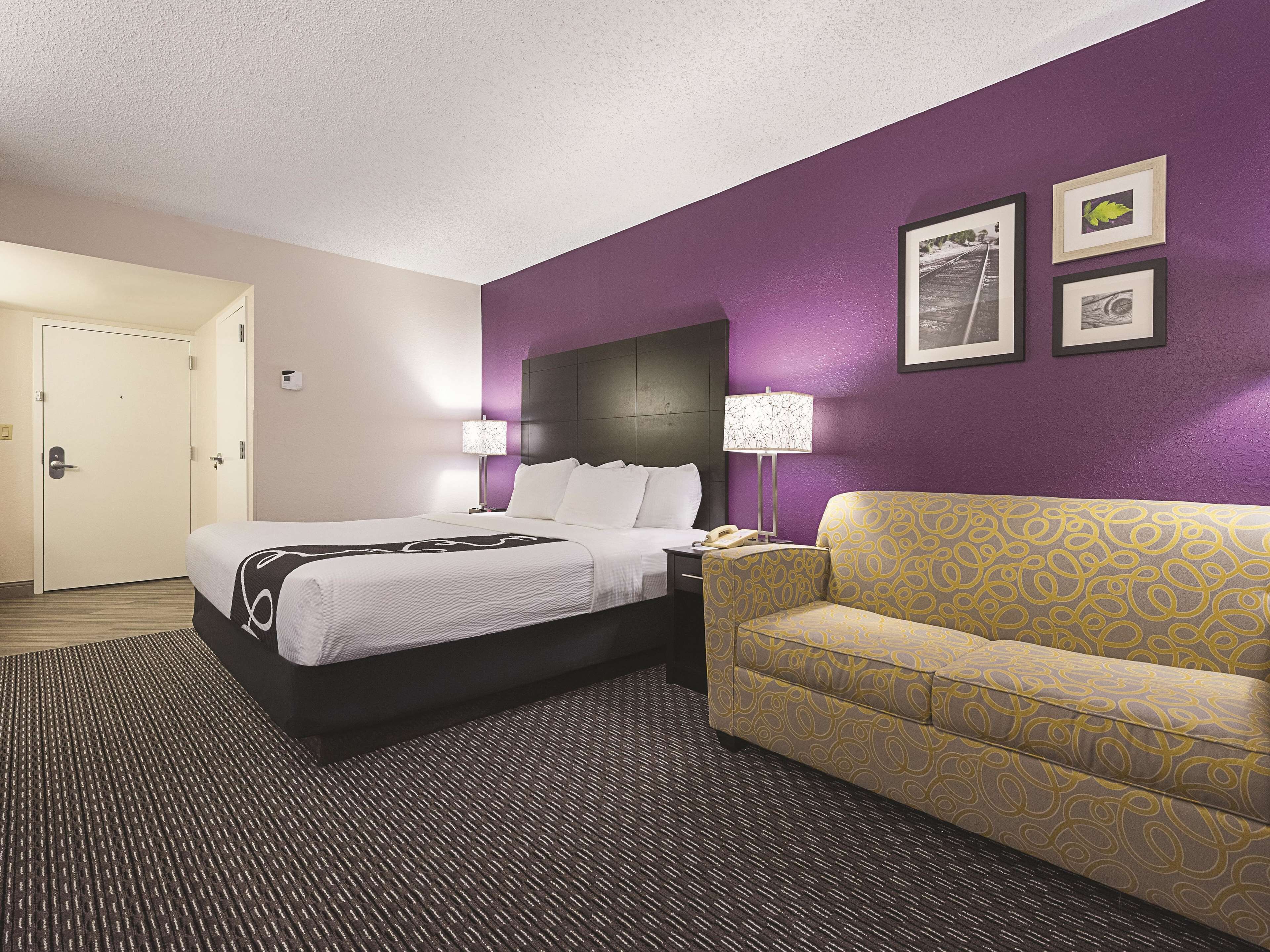 A hotel room with a bed, a sofa, a nightstand, and a lamp.