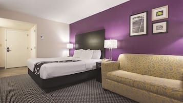 A hotel room with a bed, a sofa, a nightstand, and a lamp.