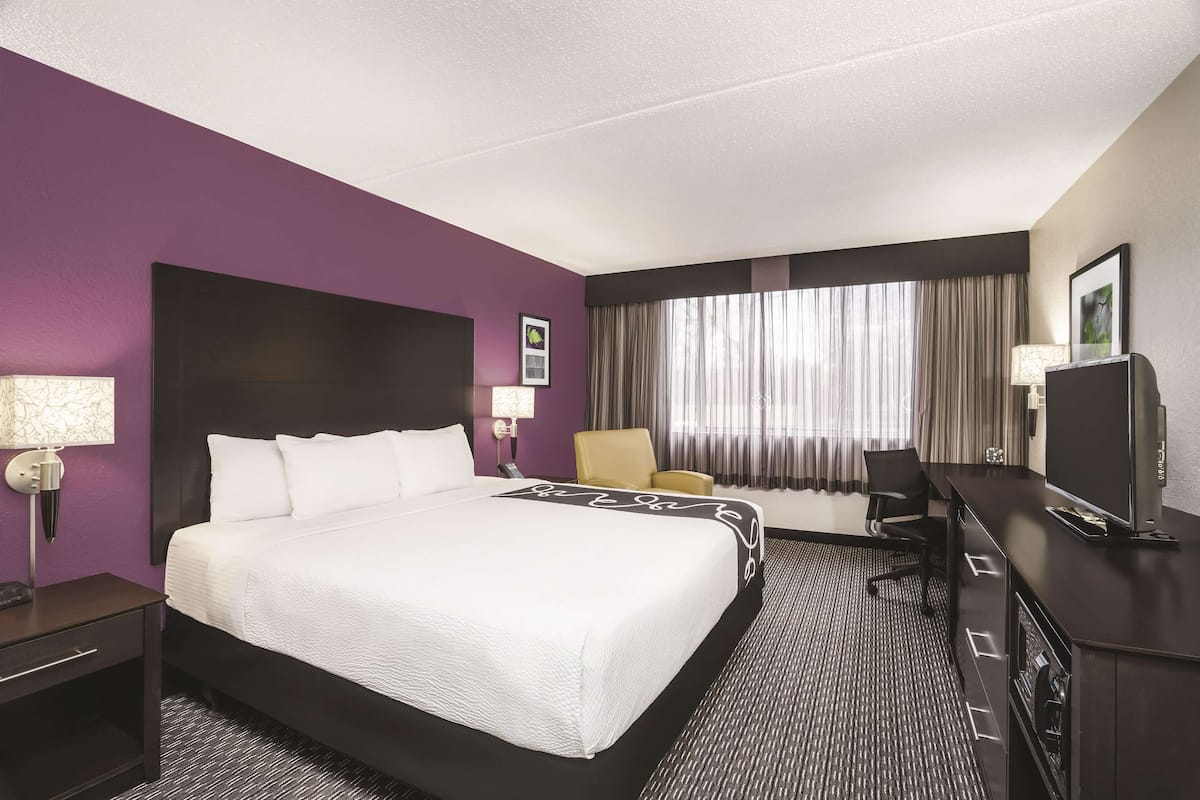 A hotel room with a large bed, a desk, a chair, and a television.
