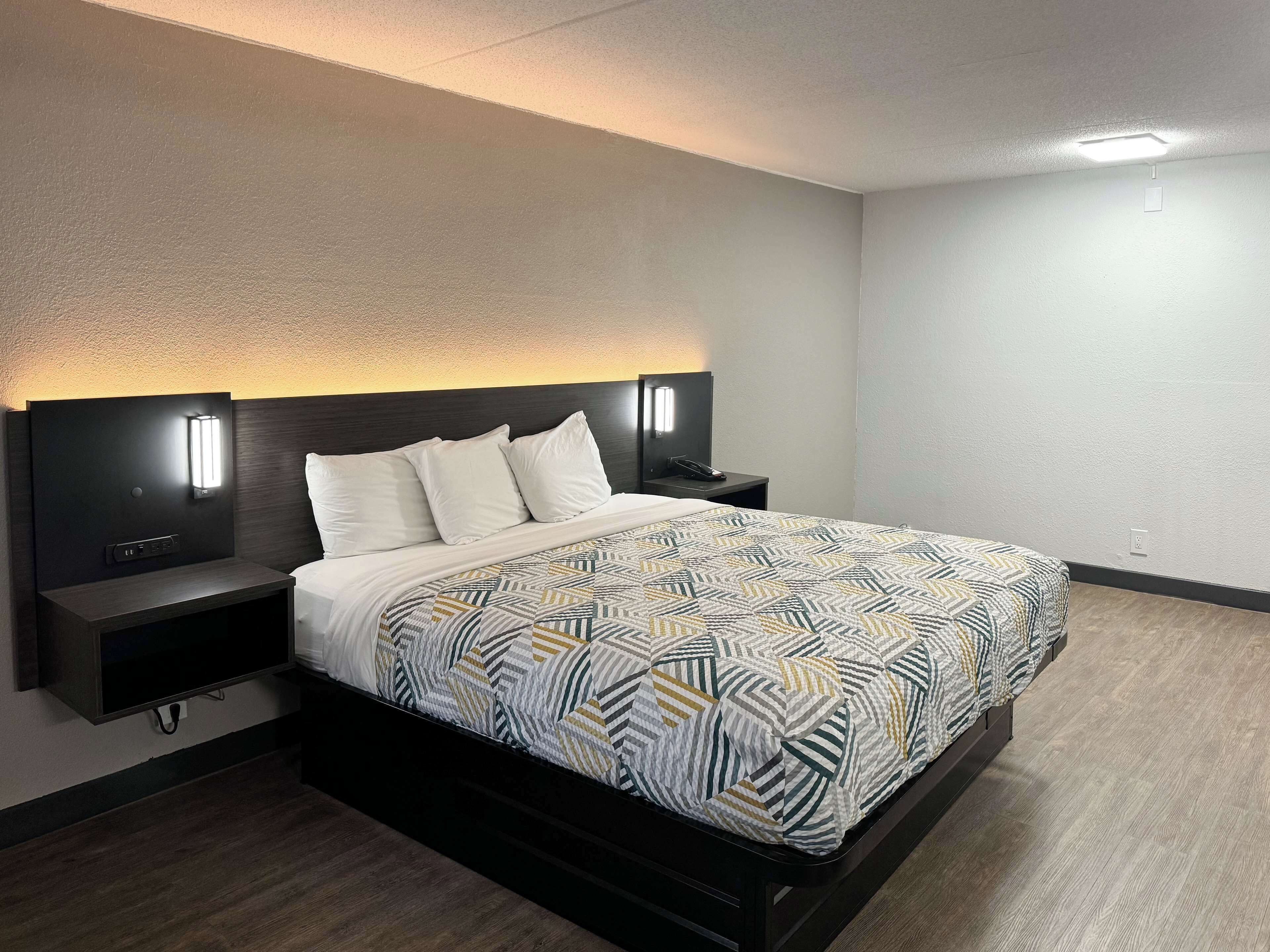 A modern hotel room with a large bed, a bedside table, and a nightstand.