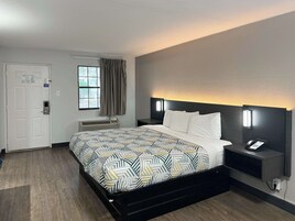 A hotel room with a bed, a bedside table with a phone, a wall-mounted light, and a window with curtains.