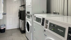 Un espace buanderie comprenant un lave-linge et un sèche-linge à chargement frontal, une poubelle et une porte donnant sur la pièce adjacente.