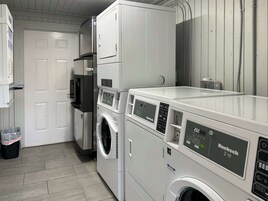 A laundry area with a front-loading washer and dryer, a trash bin, and a door to the adjacent room.