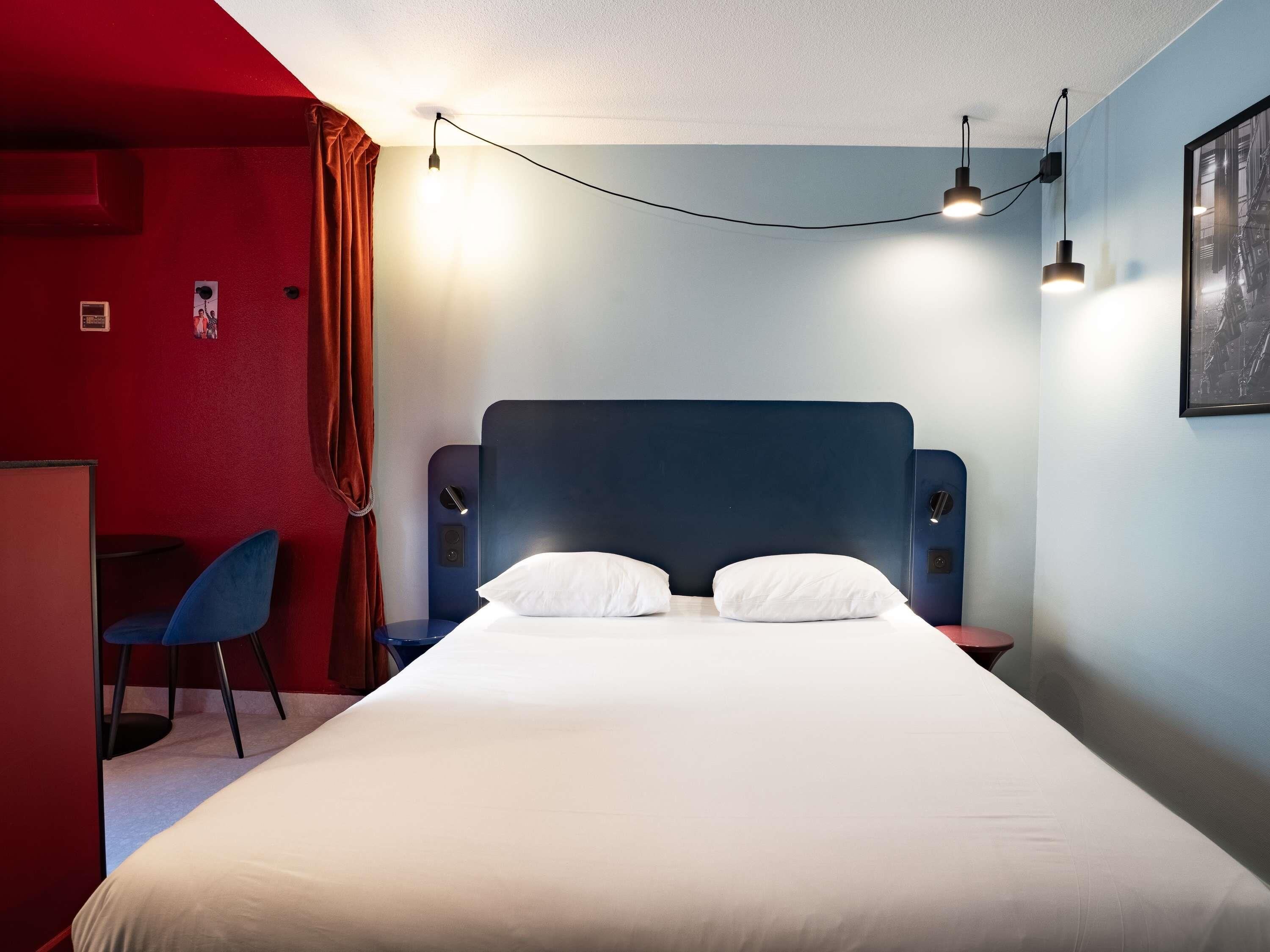 Ein Hotelzimmer mit einem großen Bett, einem Schreibtisch und einem Stuhl. Über dem Bett befinden sich Wandlampen.