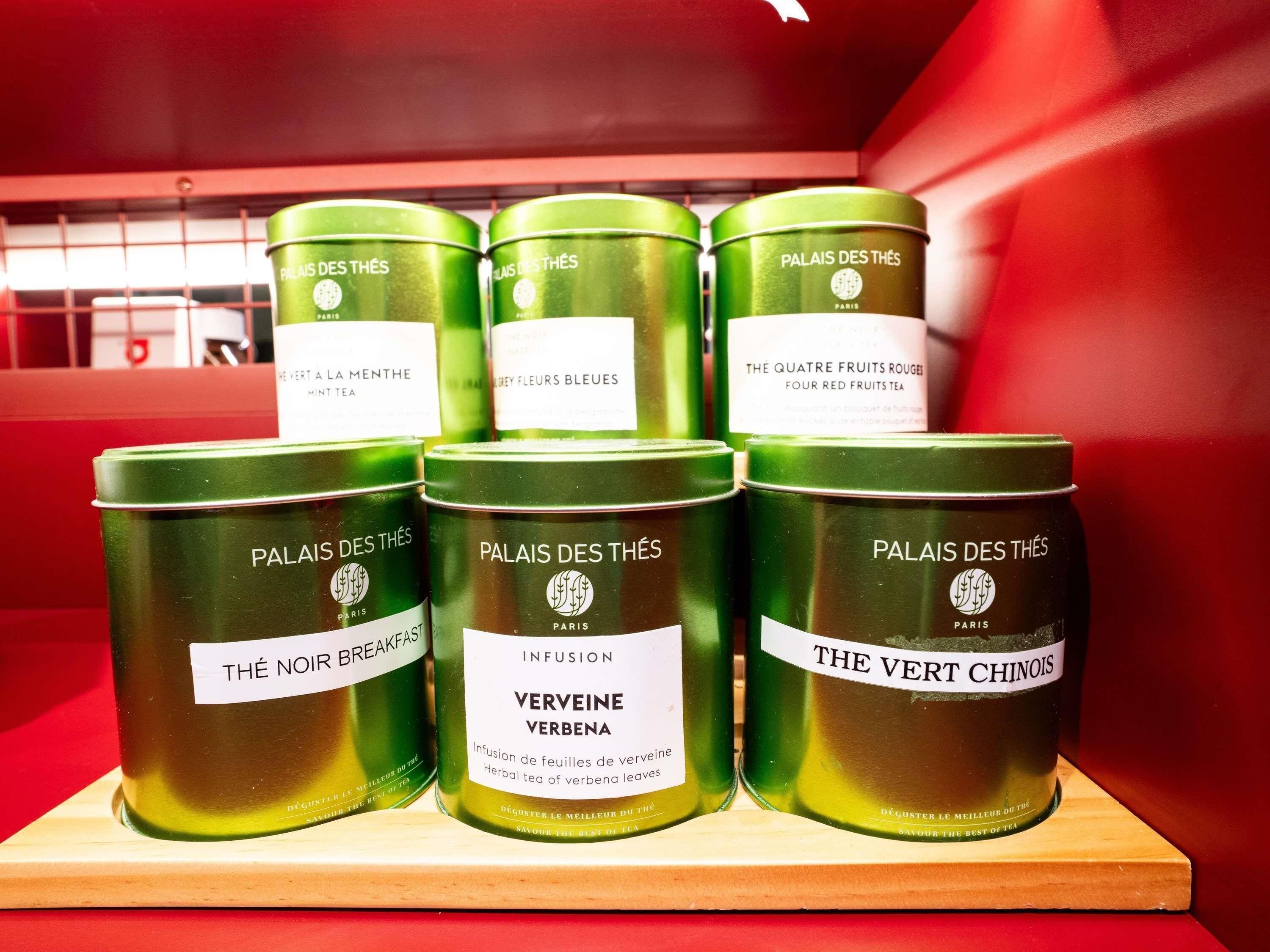 Exhibición de latas de té verde con etiquetas, dispuestas sobre un estante de madera sobre un fondo rojo.