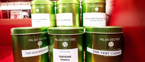 Exhibición de latas de té verde con etiquetas, dispuestas sobre un estante de madera sobre un fondo rojo.