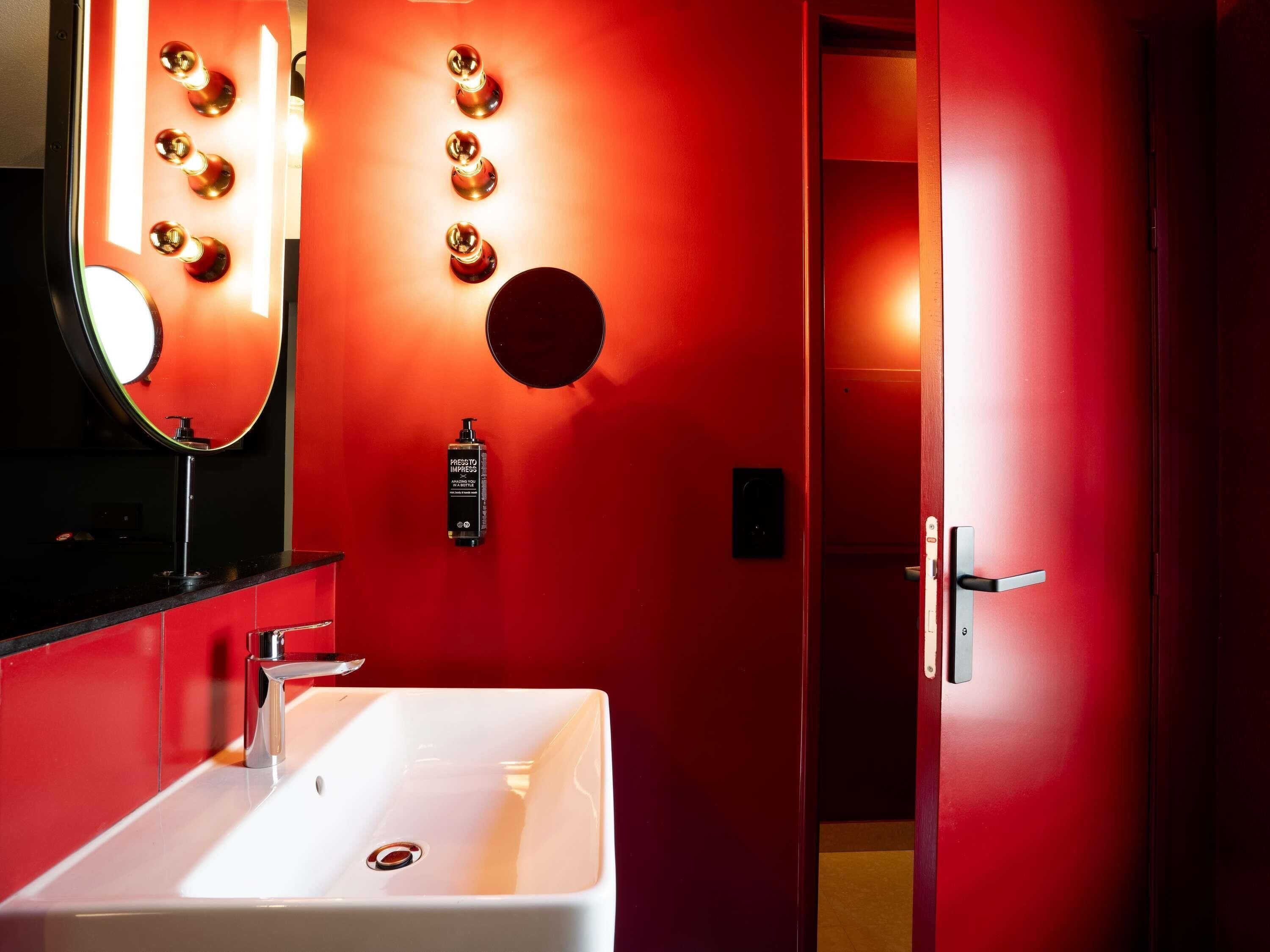 A bathroom with a white sink, a mirror, and a red wall with lights.