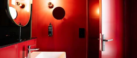 A bathroom with a white sink, a mirror, and a red wall with lights.
