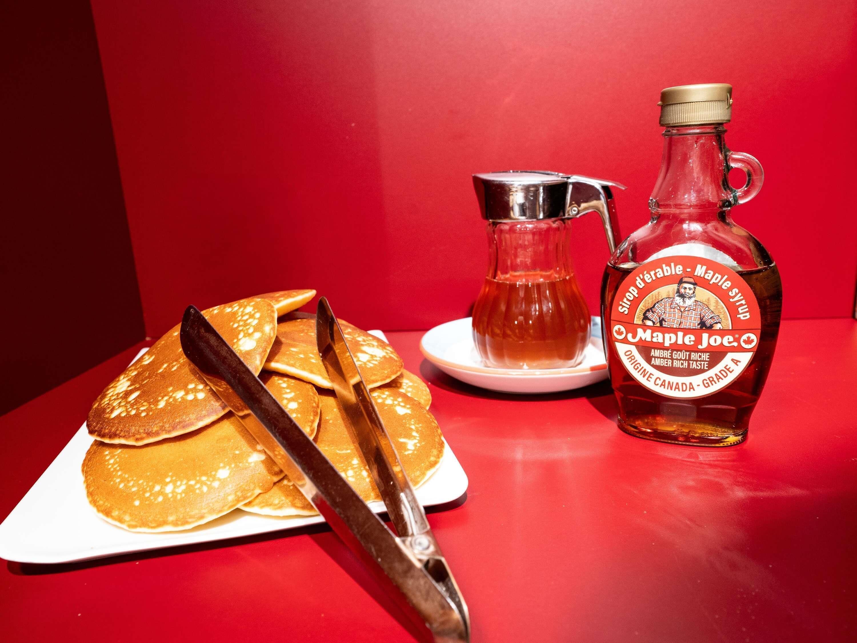 Pancakes on a plate with syrup and a bottle of maple syrup.
