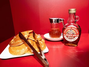 Des crêpes servies dans une assiette, accompagnées de sirop et d’une bouteille de sirop d’érable.