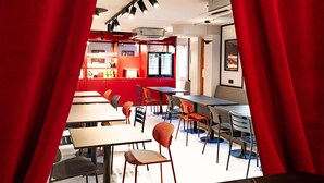 A modern restaurant with red accents, multiple seating areas, and a visible kitchen area. - ibis Styles Bourg en Bresse Centre (Bourg-en-Bresse)