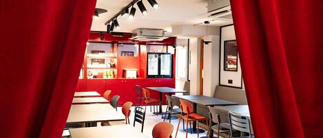 A modern restaurant with red accents, multiple seating areas, and a visible kitchen area.