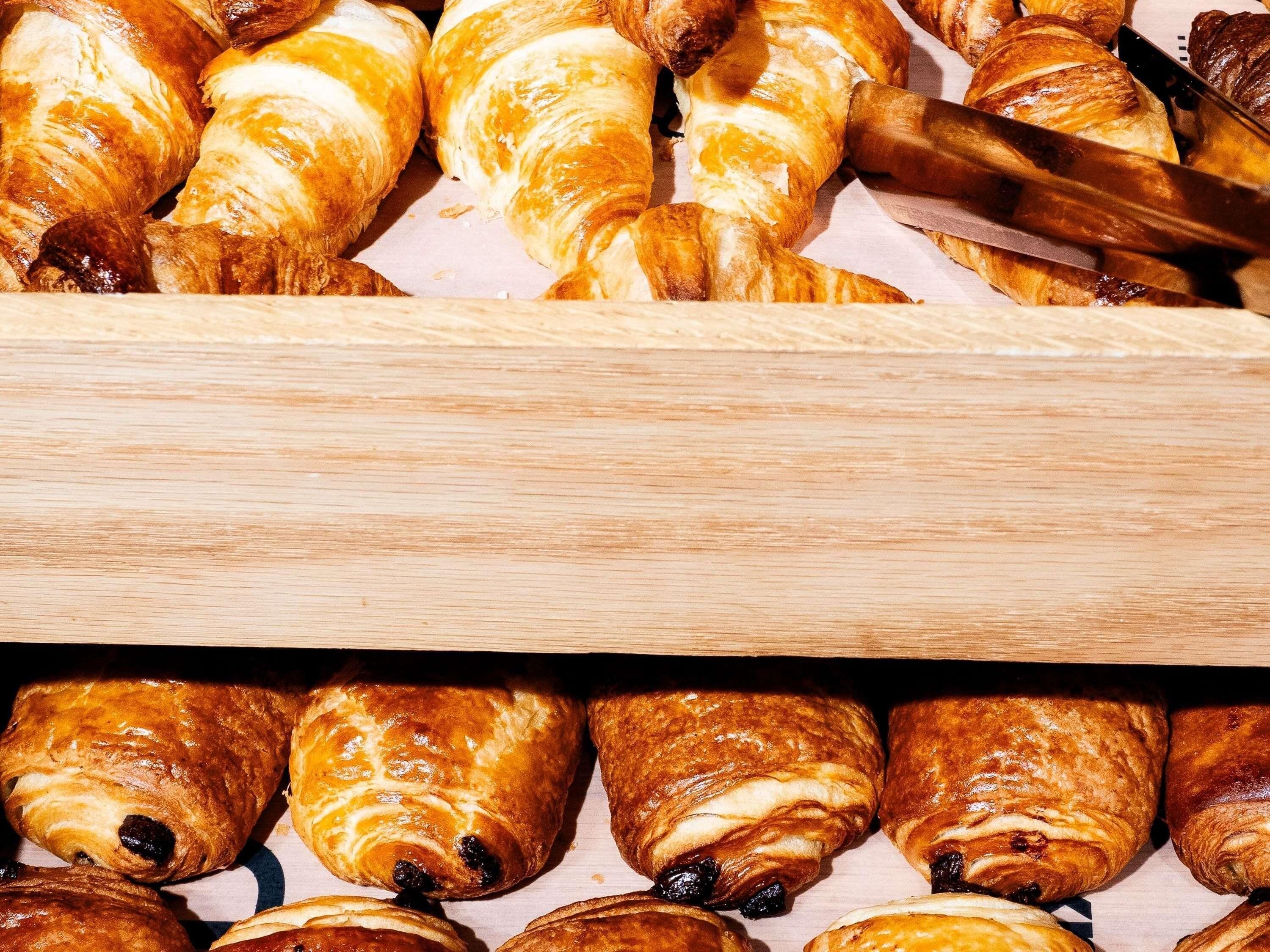 Variedad de pasteles, incluyendo croissants y medialunas de chocolate, expuestos sobre una superficie de madera.