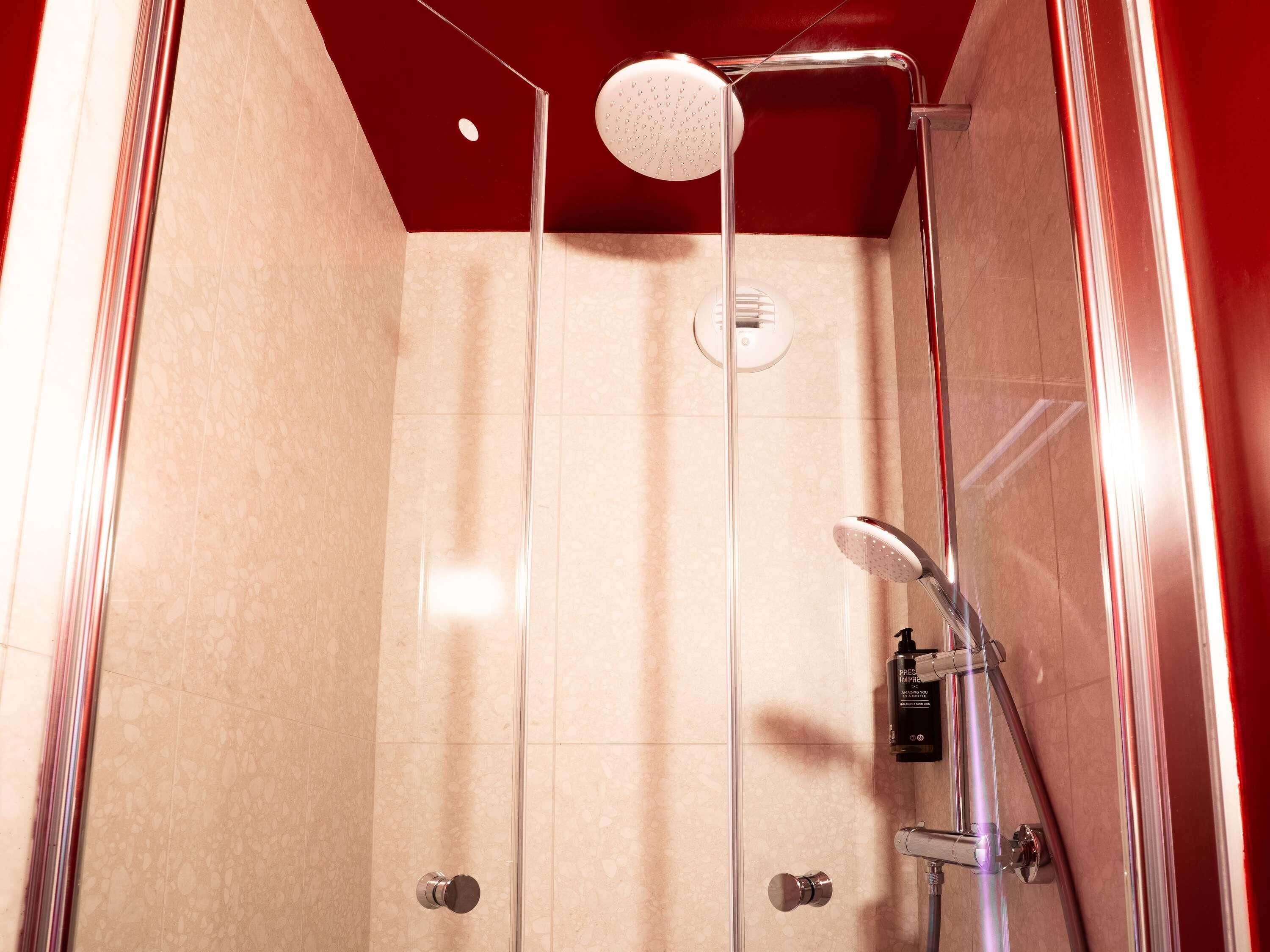 A glass-enclosed shower with a handheld showerhead and a wall-mounted faucet.