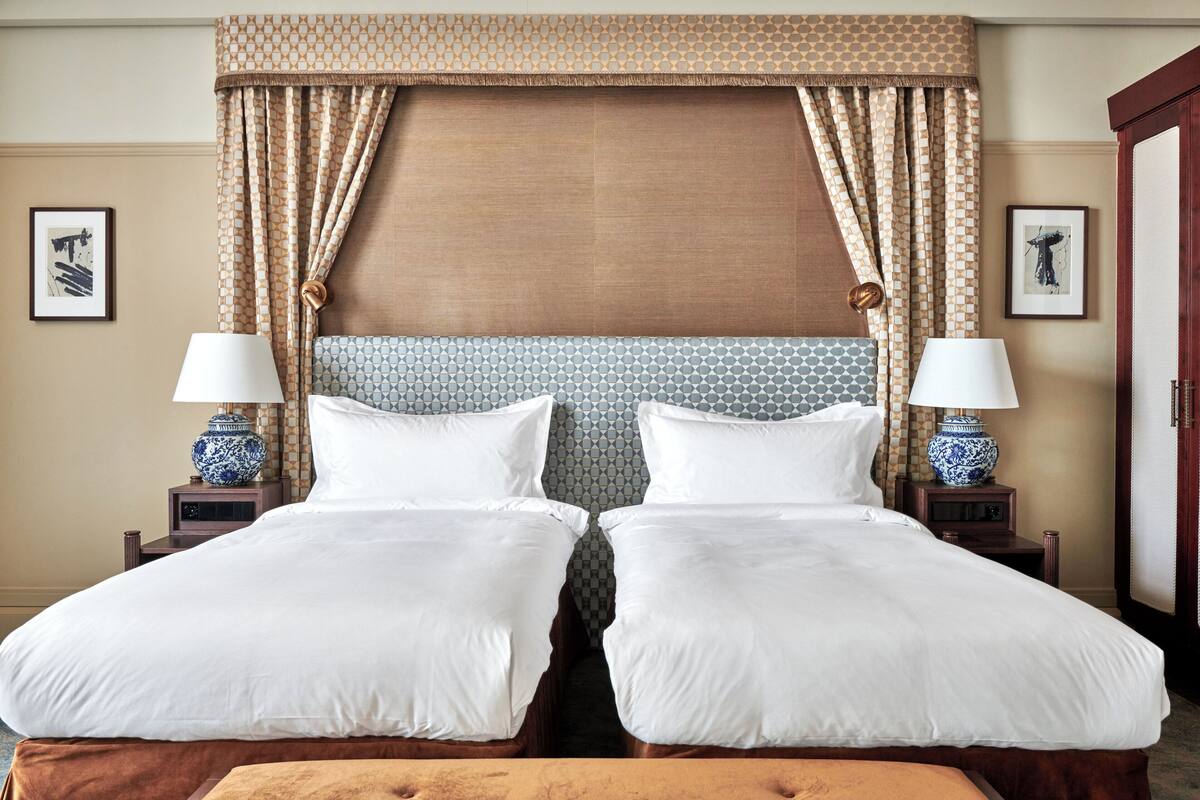 A double bed with white linens, two bedside tables with lamps, patterned curtains, and framed artwork on the walls.