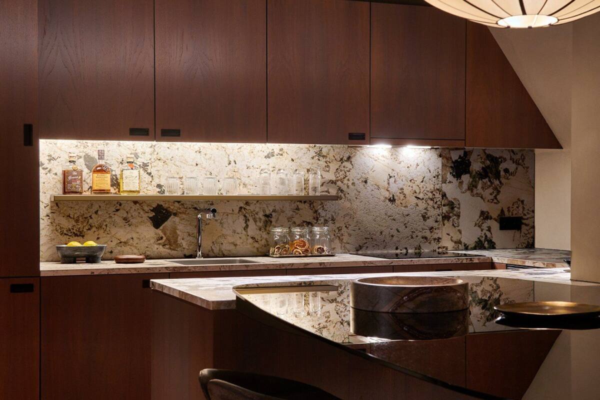 A modern kitchen with dark wood cabinets, a marble backsplash, and a central island with a sink.