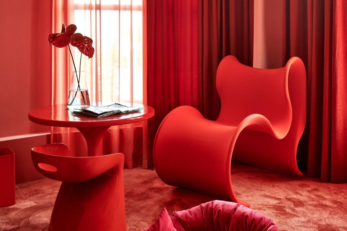 A modern room with a red color scheme, featuring a round table with a vase of flowers, a unique red chair, and a red bean bag.