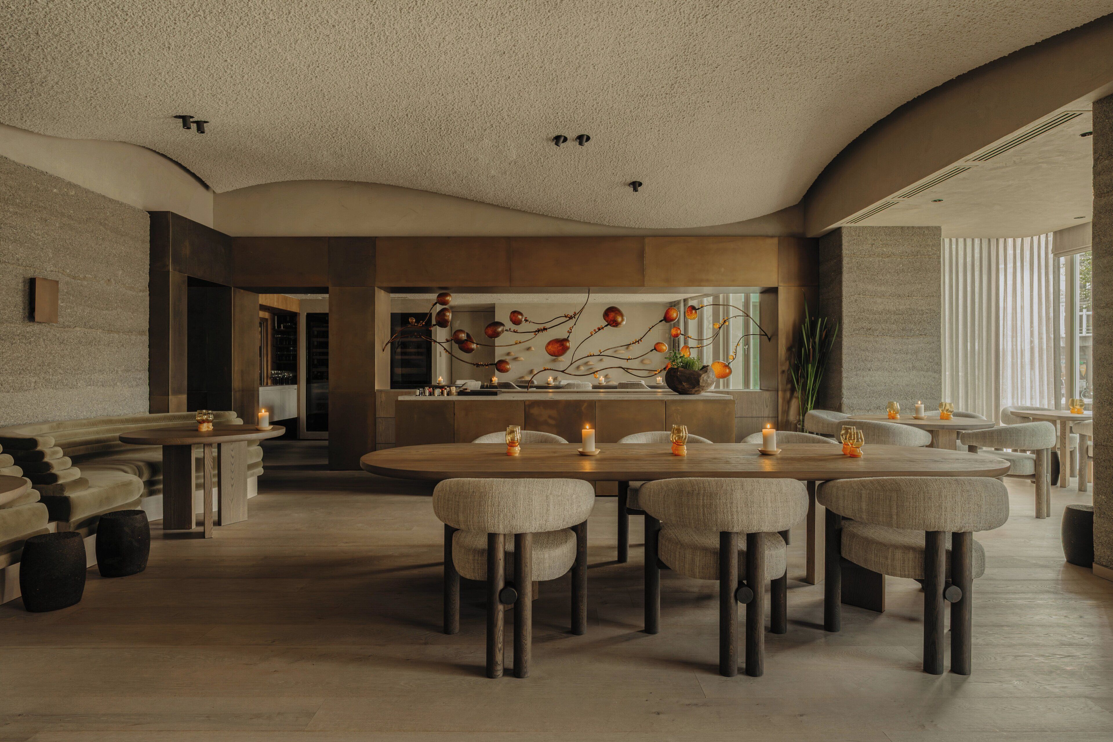 Un espace de restauration moderne avec des tables rondes et des chaises rembourrées, une pièce décorative centrale et une vue sur l’extérieur.