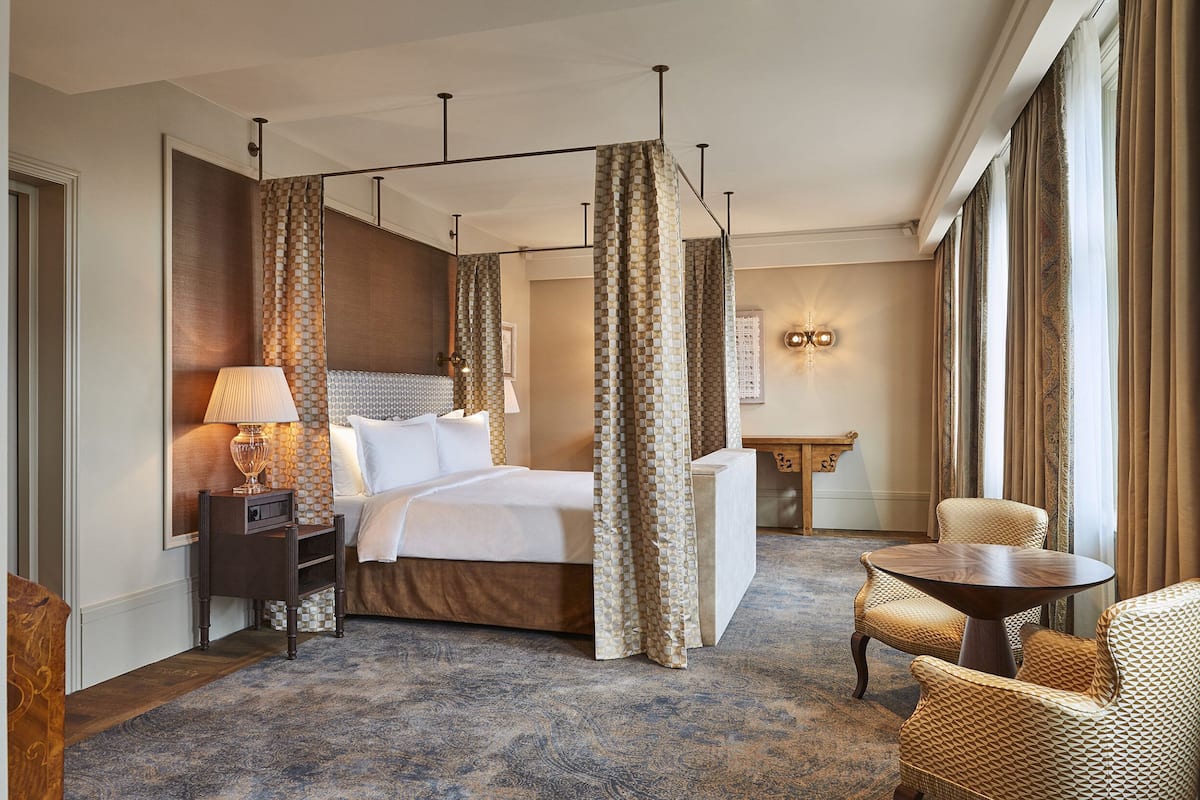 Een hotelkamer met een groot bed, een nachtkastje met een lamp, een stoel, een klein tafeltje en uitzicht op het landschap door het raam.