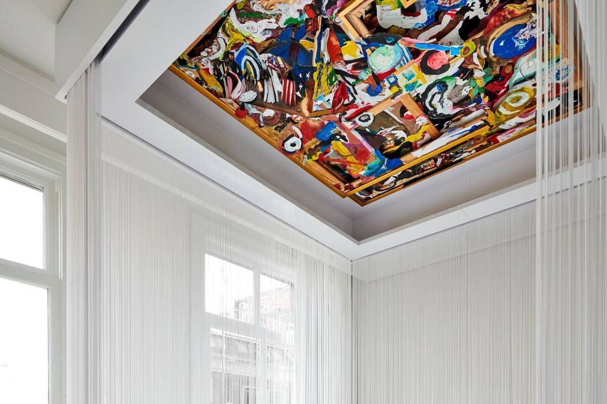 A modern bedroom with a large window, white curtains, and a colorful ceiling mural.