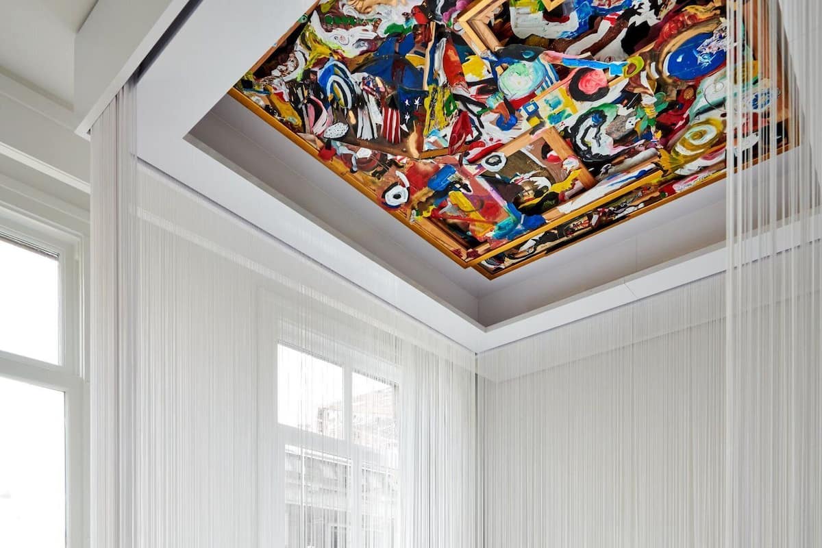 A modern bedroom with a large window, white curtains, and a colorful ceiling mural.