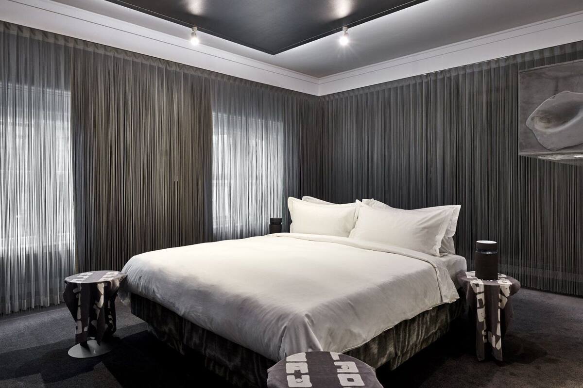 A modern bedroom with a large bed, dark curtains, and a minimalist design.