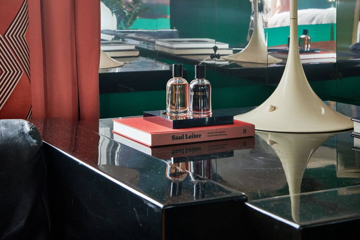 A room with a reflective surface, a white lamp, and two perfume bottles on a red box.