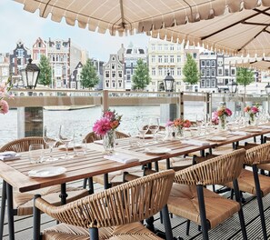 Un tavolo da pranzo apparecchiato con sedie, vista su un fiume e edifici sullo sfondo.