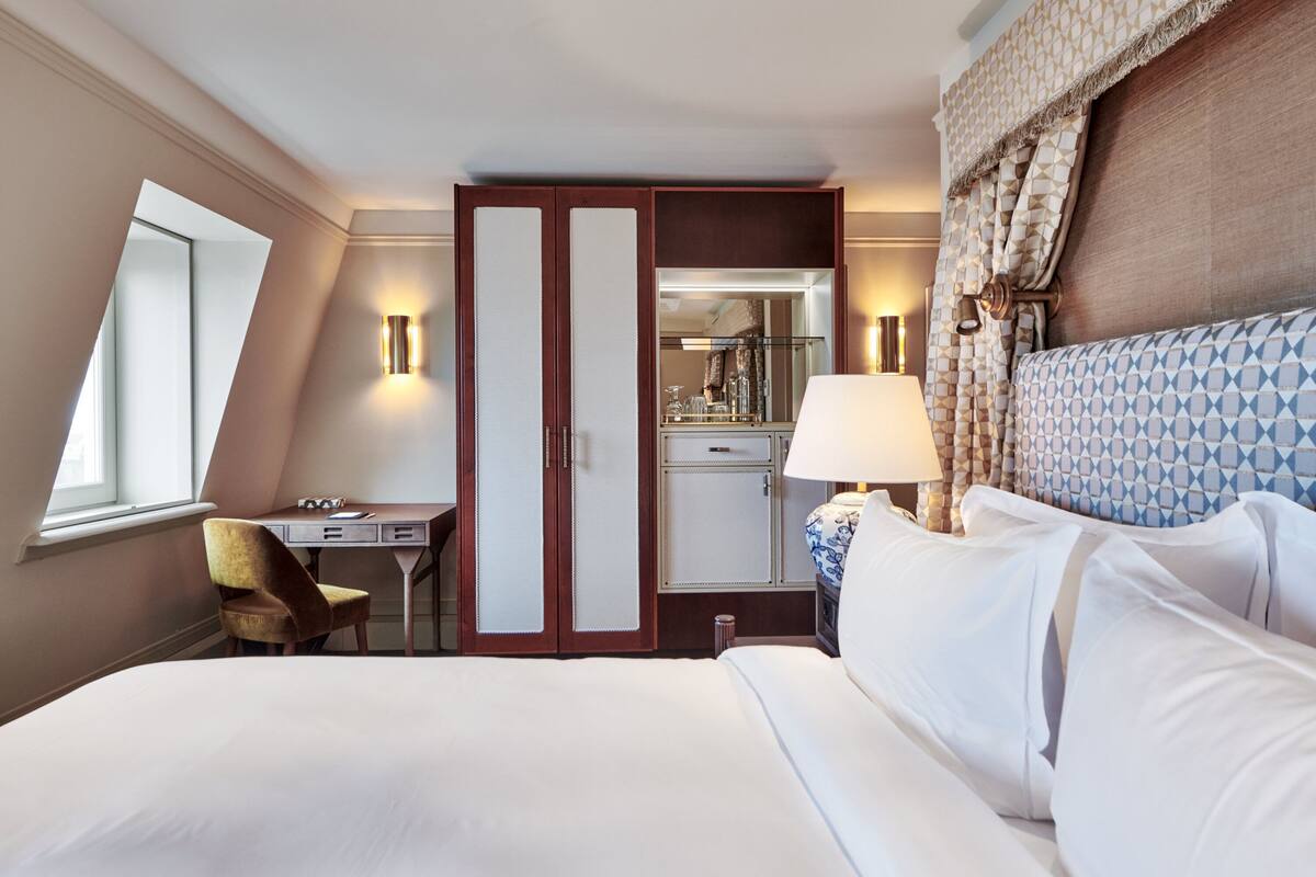 A hotel room with a large bed, a desk, a chair, a wardrobe, and a mirror.