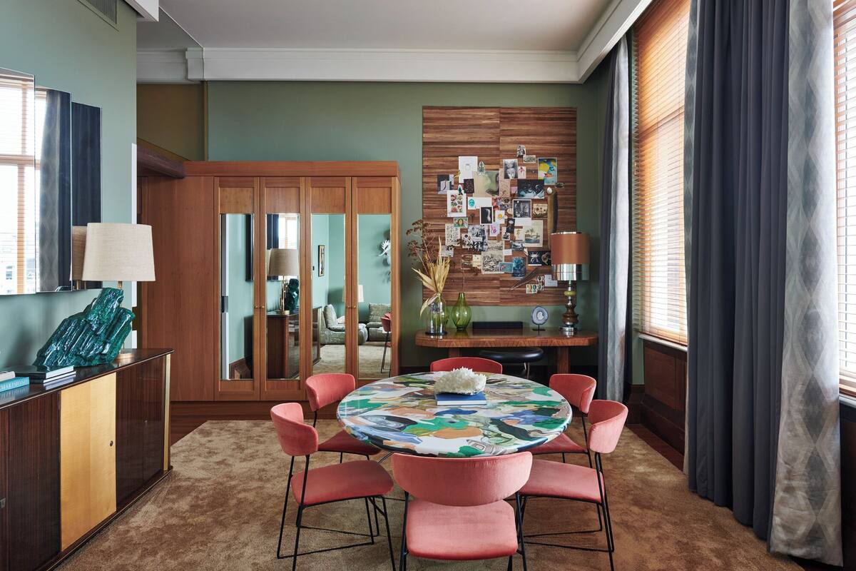 A dining area with a round table, pink chairs, and a wall decorated with photos.