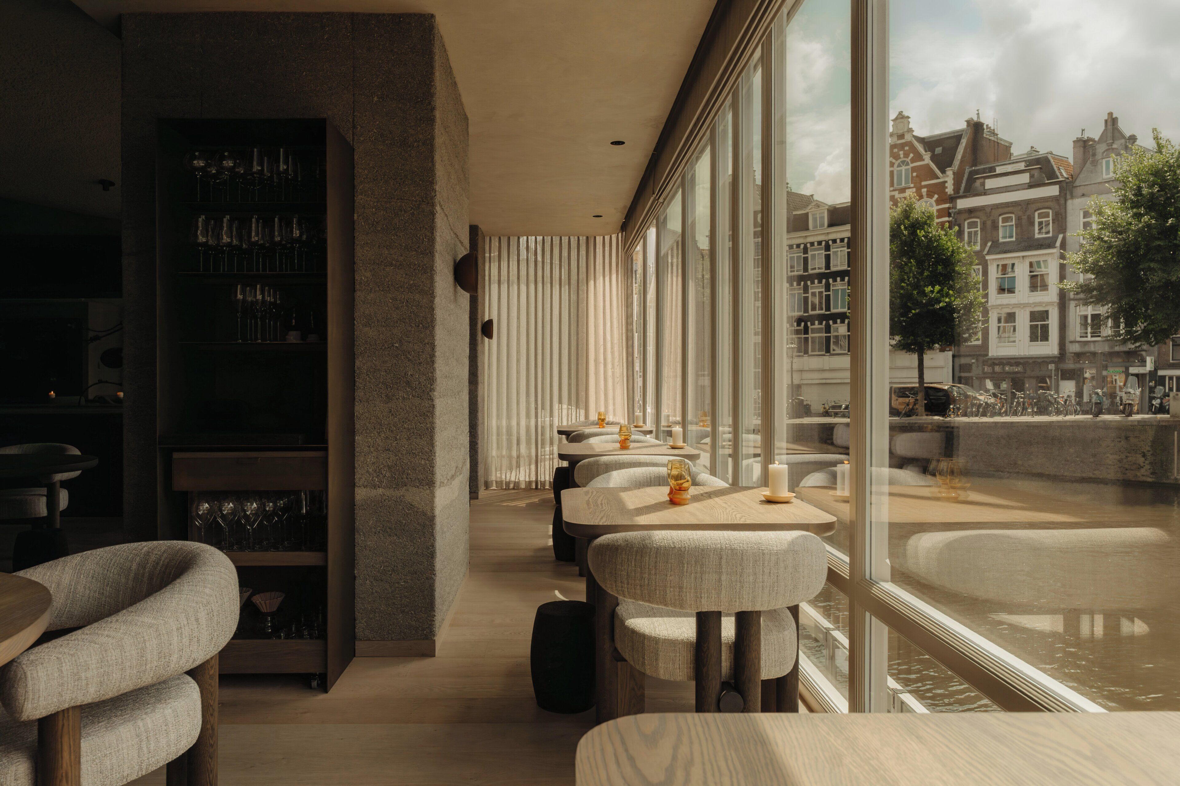 A modern interior with a bar area, seating, and a view of a canal with buildings.
